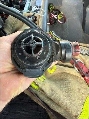 A hand holds an SCBA regulator with integrated microphones.