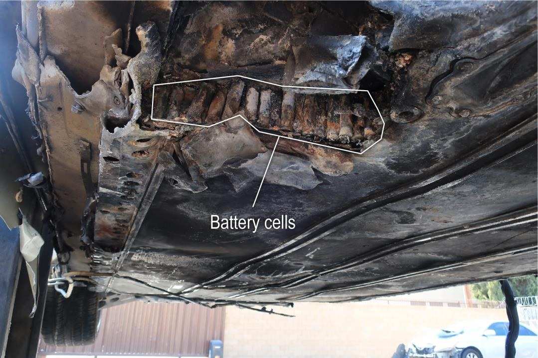 The underside of a burned SUV seen from below, with the exposed battery cells outlined and labeled.